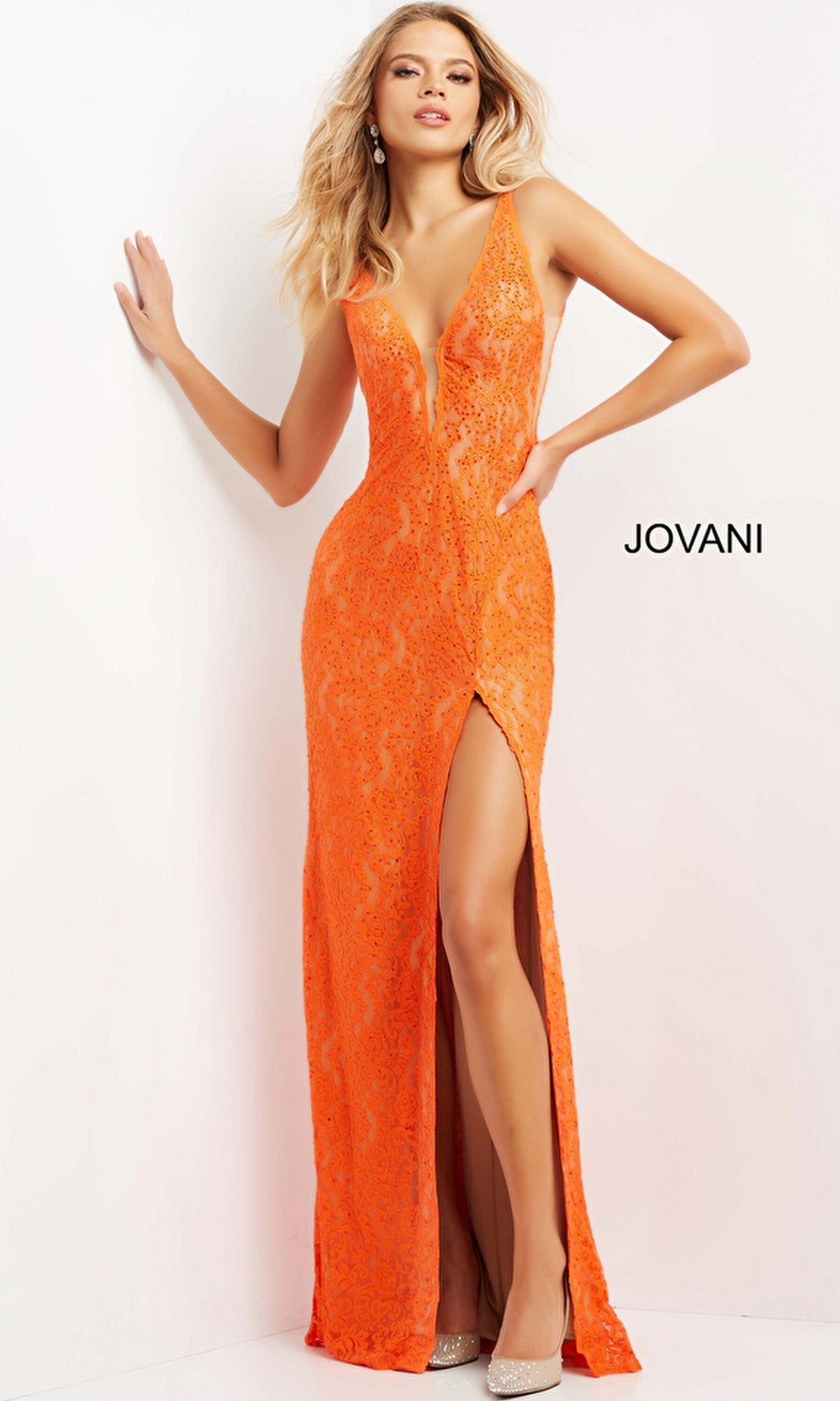 A woman poses against a white wall in Jovani Long Prom Dress 08674, featuring a sleeveless orange fitted silhouette, lace details, deep V-neckline, and thigh-high slit. The word